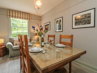 A dining area with a glass topped wooden table set with plates glasses and cutlery next to a sofa and window at Penwarne Lodge in Mawnan Smith