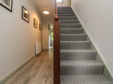 A hallway with wooden flooring and framed pictures on the wall next to a staircase with striped carpet at Penwarne Lodge in Mawnan Smith