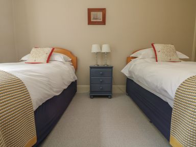 A bedroom with two single beds a blue nightstand with lamps and a framed picture above at Penwarne Lodge in Mawnan Smith