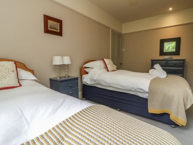 A bedroom with two single beds bedside table with lamps and a chest of drawers with a mirror at Penwarne Lodge in Mawnan Smith