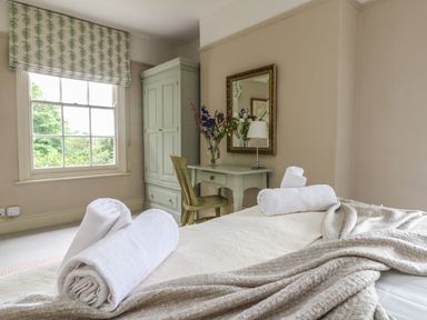 A bedroom with a bed with rolled towels a blanket a desk with flowers a chair a wardrobe and a window at Penwarne Lodge in Mawnan Smith