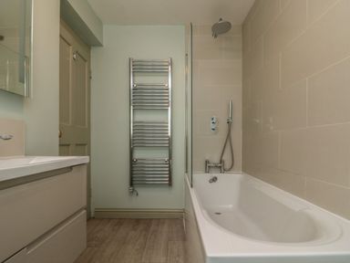 A bathroom with a bathtub shower combination a towel radiator and a sink unit at Penwarne Lodge in Mawnan Smith