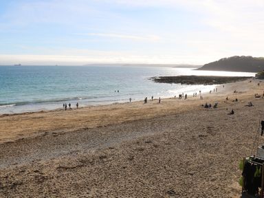 A sandy beach with people walking and sitting near the shore and a hill in the background at Penwarne Lodge in Mawnan Smith