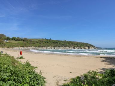 A sandy beach with a green hillside and ocean waves at Penwarne Lodge in Mawnan Smith