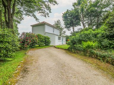 A white two story house with a gravel driveway and surrounding greenery at Penwarne Lodge in Mawnan Smith