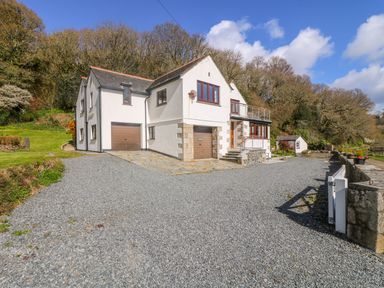 A house with garages and windows surrounded by gravel driveway and trees at Carne Mill in Manaccan