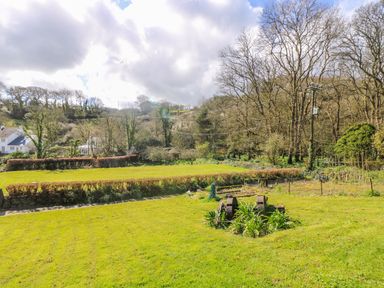A garden with grass, hedges, trees, and a sculpture at Carne Mill in Manaccan
