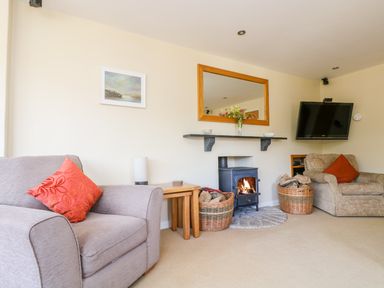 A living room with armchairs a wood-burning stove and a wall-mounted television at Carne Mill in Manaccan