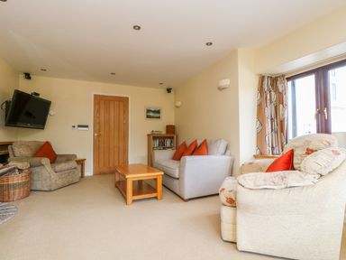 A living room with armchairs a sofa a wooden coffee table a wall-mounted tv and a window with curtains at Carne Mill in Manaccan