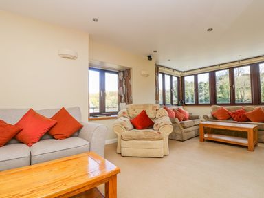 A living room with sofas and armchairs with red cushions and wooden coffee tables at Carne Mill in Manaccan