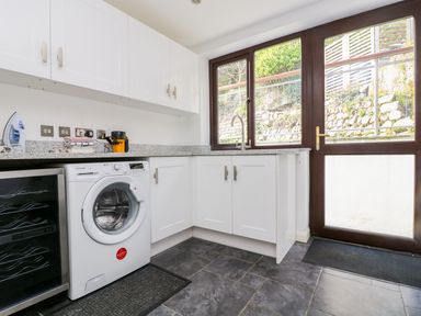 A utility room with a washing machine sink and cupboards at Carne Mill in Manaccan