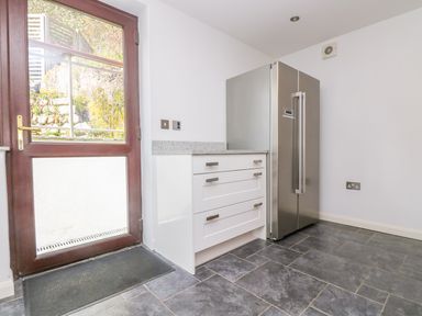 A kitchen area with a wooden door glass panel white drawers and a stainless steel refrigerator at Carne Mill in Manaccan