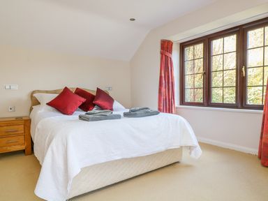 A bedroom with a double bed red pillows wooden nightstand and window with red curtains at Carne Mill in Manaccan