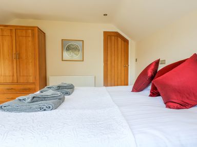 A bedroom with a white bedspread red pillows gray towels wooden wardrobe and wooden door at Carne Mill in Manaccan