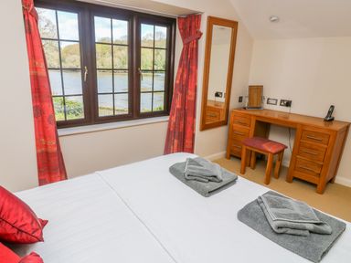 A bedroom with a bed with folded towels a wooden desk with a stool a mirror and a window with a view of trees and water at Carne Mill in Manaccan