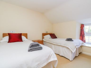 A bedroom with two single beds red pillows folded towels and a window with red curtains at Carne Mill in Manaccan