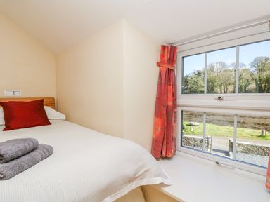 A bedroom with a bed towels on it and a window with red curtains overlooking a garden at Carne Mill in Manaccan