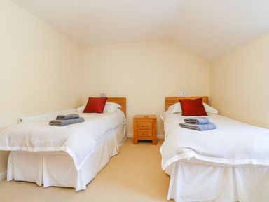A bedroom with two single beds towels and red pillows with a wooden nightstand between the beds at Carne Mill in Manaccan