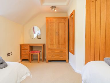 A bedroom with two single beds a wooden wardrobe a wooden dressing table with stool and a wall mirror at Carne Mill in Manaccan