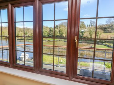 A view of a river and trees through brown framed windows at Carne Mill in Manaccan