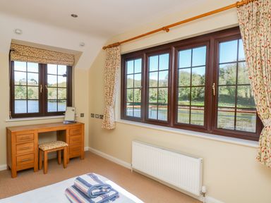 A bedroom with wooden dressing table and windows showing a lake at Carne Mill in Manaccan