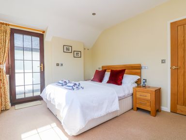 A bedroom with a bed with white bedding and red pillows next to a wooden nightstand and a door with glass panels at Carne Mill in Manaccan