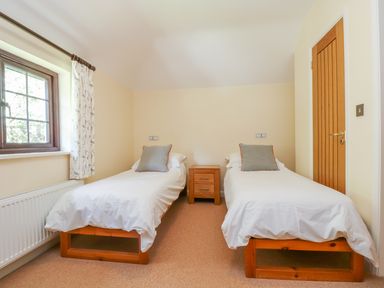 A bedroom with two single beds a wooden nightstand and a window with patterned curtains at Carne Mill in Manaccan