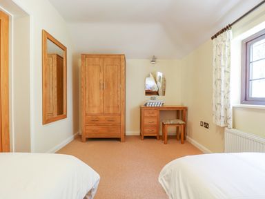 A bedroom with two beds a wooden wardrobe a dressing table with a mirror and a window with curtains at Carne Mill in Manaccan
