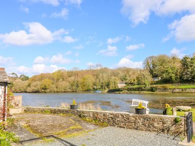 A riverside view with a stone wall planter and a small boat at Carne Mill in Manaccan