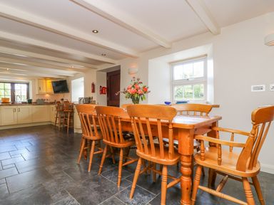 A kitchen and dining area with a wooden table and chairs and white cabinets at Carne Mill in Manaccan