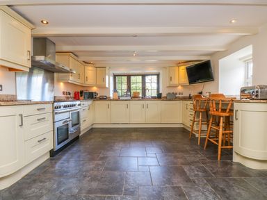 A kitchen with cream cabinets stove and chairs at Carne Mill in Manaccan