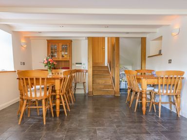 A dining room with two wooden tables and chairs a wooden cabinet and stairs at Carne Mill in Manaccan