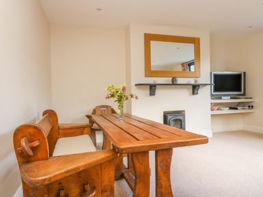 A dining area with a wooden table and benches a mirror above a fireplace and a TV on corner shelves at Carne Mill in Manaccan