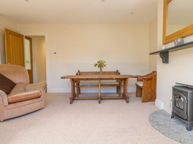 A room with a wooden table and bench with flowers on it a beige armchair a small wood stove and a mirror on the wall at Carne Mill in Manaccan