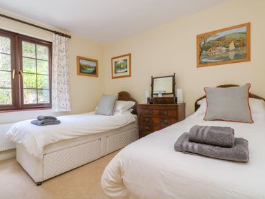 A bedroom with two single beds white bedding wooden chest of drawers and framed pictures on walls at Carne Mill in Manaccan