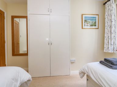 A bedroom with white built in wardrobe two beds with white bedding wall mirror and framed picture at Carne Mill in Manaccan