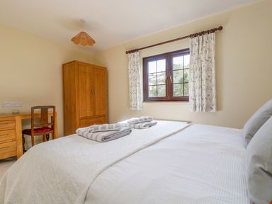 A bedroom with a double bed two towels on the bed a wooden wardrobe and a desk with a chair at Carne Mill in Manaccan