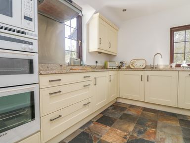 A kitchen with cream cabinets a built in oven microwave granite countertops a toaster kettle and a window at Carne Mill in Manaccan