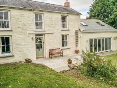 A white stone house with green door and windows garden patio bench and potted plants at Little Chycoose in Truro