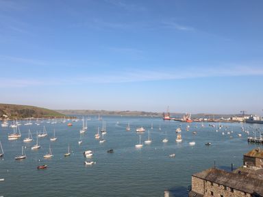 A harbor with numerous sailboats and some industrial cranes in the background at Little Chycoose in Truro