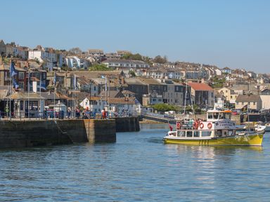 A harbor with a yellow ferry boat and buildings on a hill at Little Chycoose in Truro