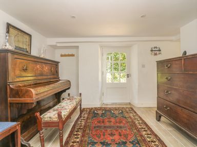 A room with a wooden piano and bench a wooden chest of drawers and a door with glass panels at Little Chycoose in Truro