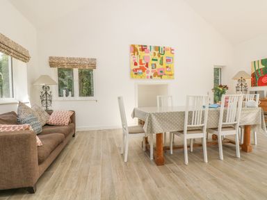 A dining room with a table covered by a polka dot tablecloth surrounded by white chairs next to a brown sofa with patterned cushions at Little Chycoose in Truro