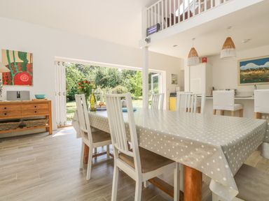 A dining room with a table covered with a polka dot tablecloth and white chairs next to an open door to a garden at Little Chycoose in Truro