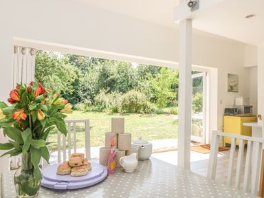 A dining area with a table set with scones cups a teapot and flowers overlooking a garden at Little Chycoose in Truro