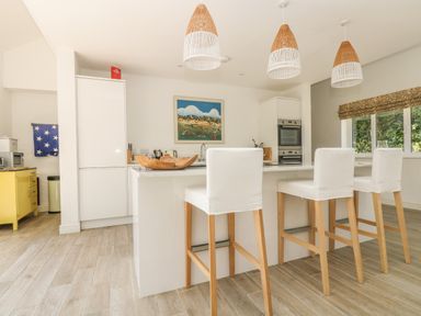 A kitchen with white cabinets a large island with three white chairs wooden pendant lights and a window with blinds at Little Chycoose in Truro