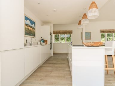 A kitchen with white cabinets wooden floor three pendant lights and a wooden bowl on the island at Little Chycoose in Truro