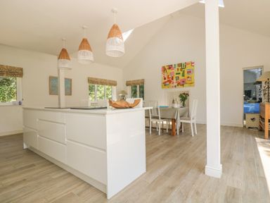 An open kitchen and dining area with a white island, wooden floor, hanging lamps, and a dining table with chairs at Little Chycoose in Truro