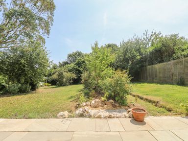 A backyard garden with a stone patio a small planted area with rocks a terracotta pot and trees at Little Chycoose in Truro