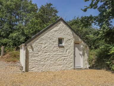 An exterior view of a small stone building with a door and window surrounded by trees at Little Chycoose in Truro